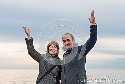 A man and a woman standing nearby raised their hands in greeting. Sea and sky in the background Stock Photo