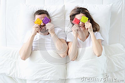 Man and woman are holding colorful condoms while lying on bed Stock Photo