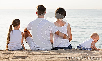 Man and woman with kids sitting with back to camera on beach Stock Photo