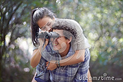 Man, woman and piggyback in forest with binocular for travel, adventure or sightseeing in nature with happiness. Couple Stock Photo