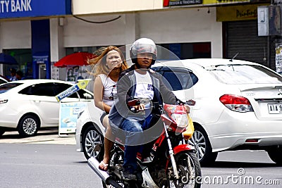 A man and a woman riding in tandem on a motorcycle in Antipolo City. Editorial Stock Photo