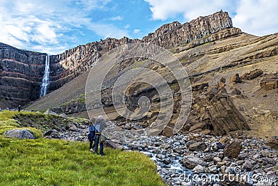 Man and woman tourists enjoying spectacular landscape around of Hengifoss waterfall and basaltic strata with thin, red and yellow Editorial Stock Photo