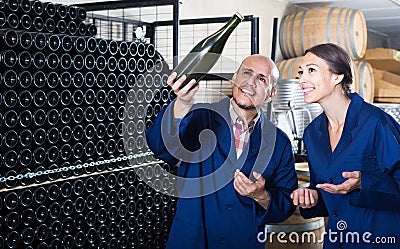 man and women coworkers looking at bubbly wine in bottle standing in wine cellar Stock Photo