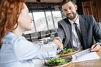 Businesspeople having business lunch at restaurant sitting eating salad drinking wine shaking hands making deal happy Stock Photo