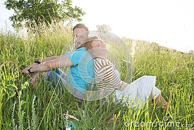 Portrait of carefree man and woman relaxing on the meadow with enjoyment. Man and woman sitting back to back each other Stock Photo