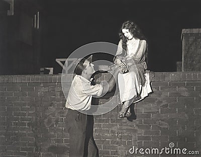 Man wooing woman sitting on brick wall Stock Photo