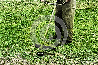 Man in work clothes mows green grass with a trimmer Stock Photo