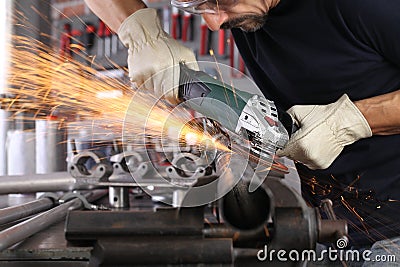 Man work in home workshop garage with angle grinder, goggles and construction gloves, sanding metal makes sparks closeup, diy and Stock Photo