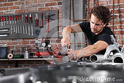 Man work in home workshop garage with steel file rasp, filing metal pipe on the workbench full of wrenches, diy and craft concept Stock Photo