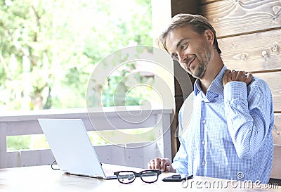 Man work on laptop on a open terrace and feelsl pain in his neck. Freelance or home office concept Stock Photo