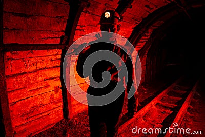 A man in work overalls and a helmet with a jackhammer on his shoulder is standing on the rails. Silhouette in red. Miner Stock Photo