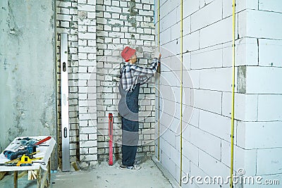 Man in work wear installing metal rails onto aerated concrete block wall Stock Photo