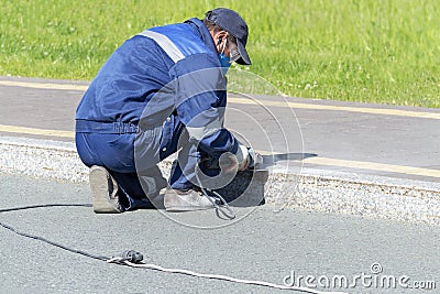 A man worker cleans a marble electric curb with an electric hand grinder. Editorial Stock Photo