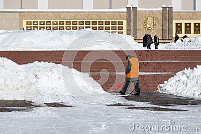Man worker of communal service in orange special clothes cleans street in center of city from snow after heavy snowfall in March Editorial Stock Photo