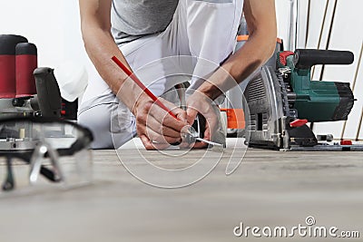 Man worker hands installing timber laminate floor, takes measurement with the tape measure and pencil. Wooden floors house renovat Stock Photo