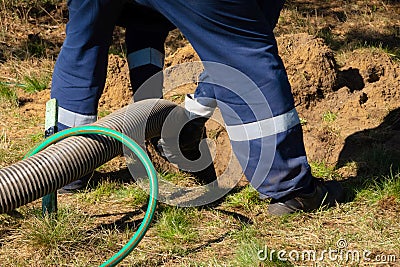 Man worker holding pipe, providing sewer cleaning service outdoor. Sewage pumping machine is unclogging blocked manhole Stock Photo
