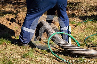 Man worker holding pipe, providing sewer cleaning service outdoor. Sewage pumping machine is unclogging blocked manhole Stock Photo