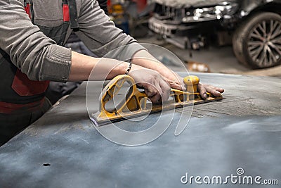 Man worker preparing for painting a car element using emery sender by a service technician leveling out before applying a primer Stock Photo