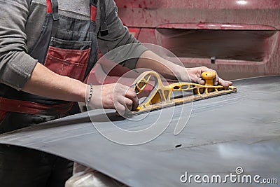 Man worker preparing for painting a car element using emery sender by a service technician leveling out before applying a primer Stock Photo