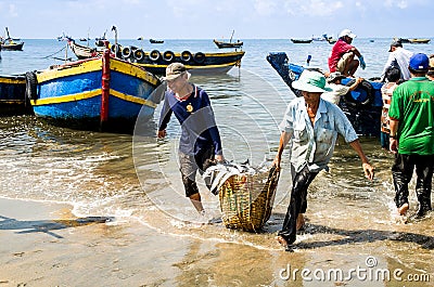 Man workers carrying deep bamboo basket loaded with fish at Long Hai fish market, Ba Ria Vung Tau province, Vietnam. Editorial Stock Photo