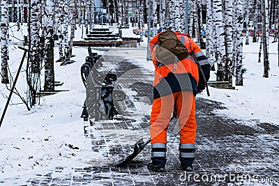 A man in working clothes with a shovel removes snow on the track in the park in winter Editorial Stock Photo