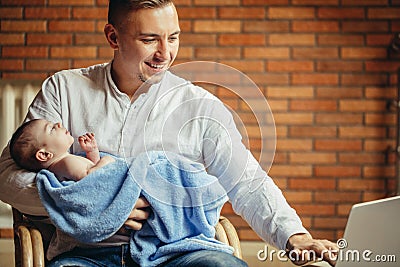 Man working at desk at home with laptop, holding cute babys, looking at screen Stock Photo