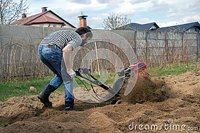 Man working in the garden with garden tiller. tractor cultivating and loosens soil field Stock Photo
