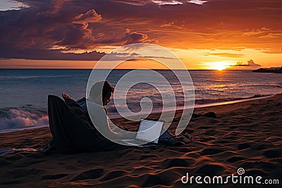 Man working on a laptop on the beach during a beautiful sunset, man lying on the sand of the beach with a laptop working at sunset Stock Photo