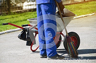 Man in a working overall with a whisk in his hand and with a garbage cart. Summer cleaning in the city Stock Photo