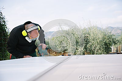 Man working with wood outdoors. Cutting board with jigsaw. PPE . eyewear, earwear and protective mask Stock Photo
