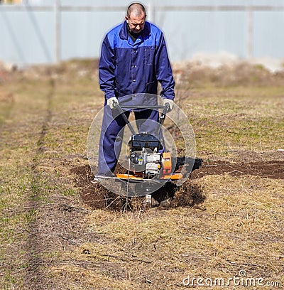 A man works in a vegetable garden in early spring. Digs the ground. Works as a cultivator, walk-behind tractor Stock Photo