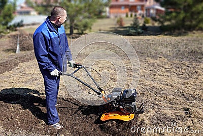 A man works in a vegetable garden in early spring. Digs the ground. Works as a cultivator, walk-behind tractor Stock Photo