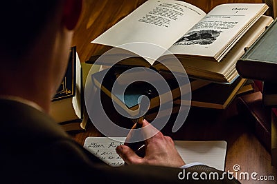 Looking over the shoulder of a man writing a letter while reading literary works Editorial Stock Photo