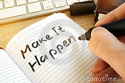 Man writing make it happen in a note. Stock Photo