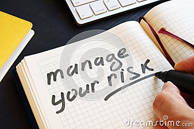 Man is writing manage your risk in a note. Stock Photo