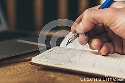 Man writing in a notebook, planning mouths with laptop in background Stock Photo