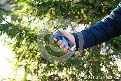 Man& x27;s hand is holding smartphone in hand on tree background outdoors. Concept of communication, call, messaging business Stock Photo