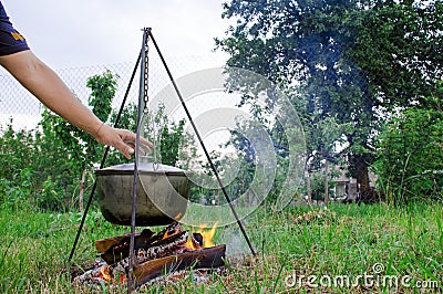 A man& x27;s hand kindles a fire under a pan, which stands on a fire Stock Photo