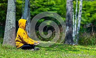 Man in yellow hoodie is relaxingly practicing meditation in the forest to attain happiness from inner peace wisdom for healthy Stock Photo