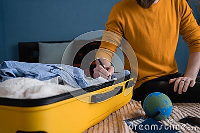 A man in a yellow sweater writes down what to take with him on a trip. Making check list of things to pack for travel Stock Photo