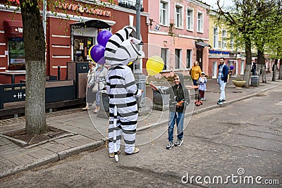 A man in a zebra costume on a city street greets passers-by and gives balloons to children. Advertising on the street Editorial Stock Photo