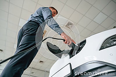 Manager is in the headphones and with notepad. Handsome car dealership worker is with electric vehicle Stock Photo