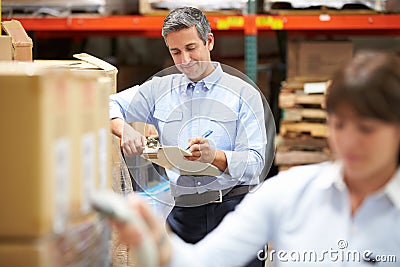 Manager In Warehouse With Worker Scanning Box In Foreground Stock Photo