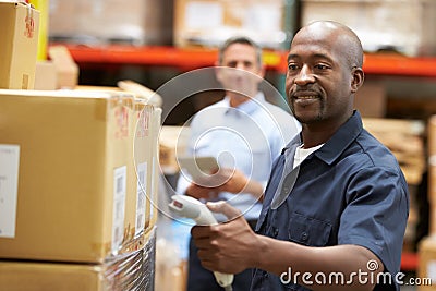 Manager In Warehouse With Worker Scanning Box In Foreground Stock Photo