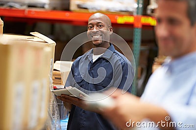 Manager In Warehouse With Worker Scanning Box In Foreground Stock Photo