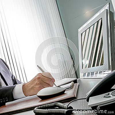 Manager at work. The expert hand of a businessman sitting at his desk, he holds the pen in front of his computer monitor that Stock Photo