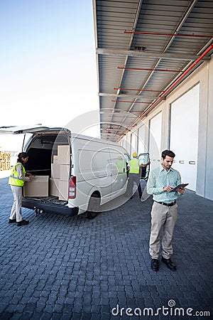 Manager working on tablet and warehouse workers loading the cardboard boxes Stock Photo