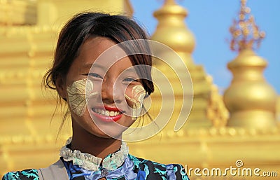 MANDALAY, MYANMAR - DECEMBER 17. 2015: Portrait of a Burmese girl with traditional Thanaka face painting in front of golden Pagoda Editorial Stock Photo