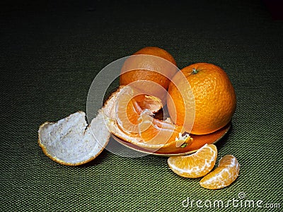 Mandarin or clementine oranges, dark still life on green. Light painting technique. Three fruit, one part peeled. Stock Photo