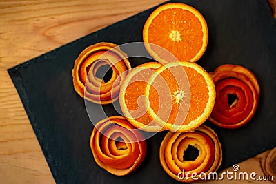 Mandarin is served on a dark stone with a decor of a peel citrus. A half tangerine and peel of spiral on a plate. Stock Photo